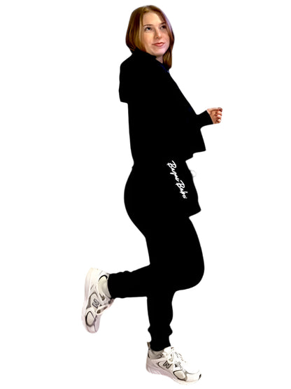 A woman wearing black joggers with a branded logo on the left leg, standing in a casual pose.