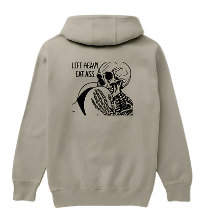 A beige hoodie with a graphic print on the back showing a stylized skeleton and text 'LIFT HEAVY EAT ASS'.